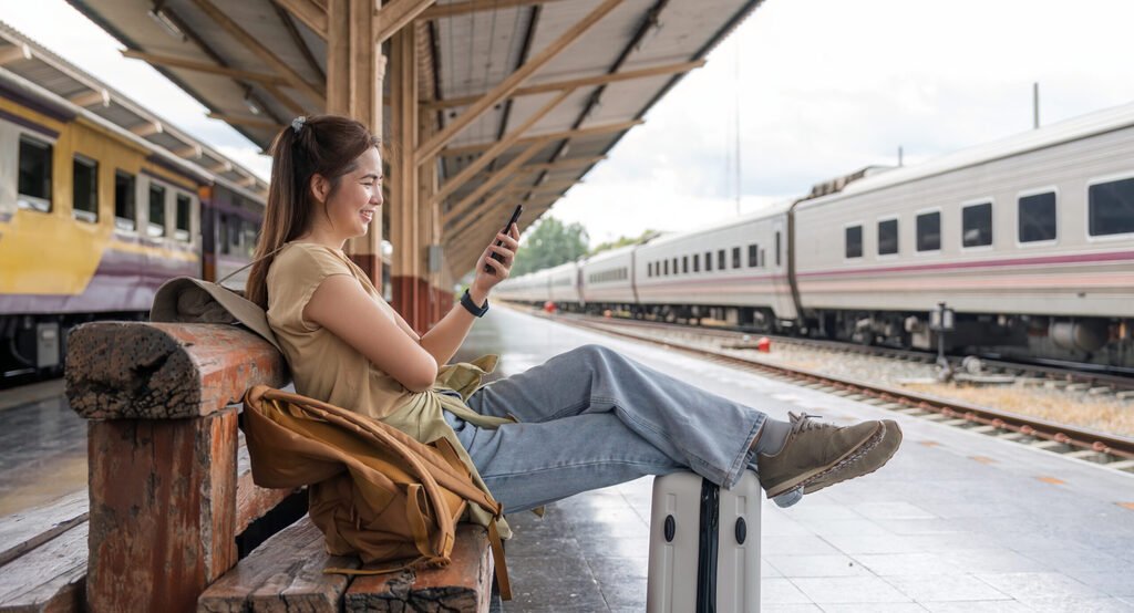 Asian female traveler using her smart phone mobile while waiting for a train at a station